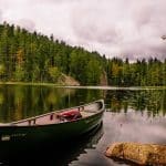 red and white canoe on lake near green trees under white clouds during daytime